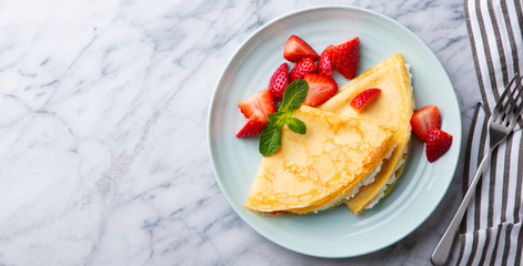 Crepes, thin pancakes with cream cheese, ricotta and fresh strawberries. Marble background. Top view. Copy space.