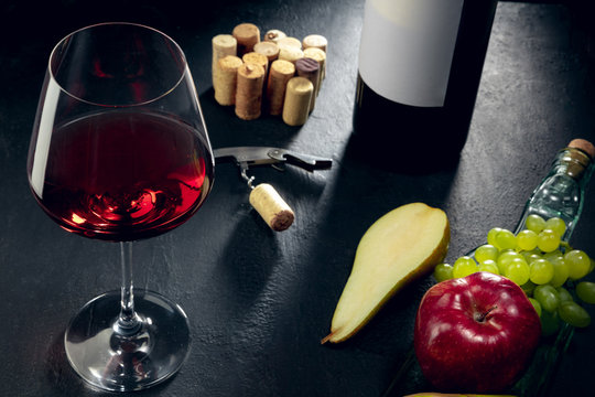 Delicisious and tasty food and drink. A bottle and a glass of red wine with fruits over dark stone background. Top view with copy space to insert your text, image or ad. Grape, apple, pear and corks.