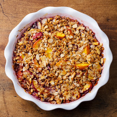 Berry, peach crumble, crisp in a baking dish. Wooden background. Top view.
