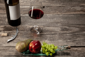 Delicisious and tasty food and drink. A bottle and a glass of red wine with fruits over weathered...
