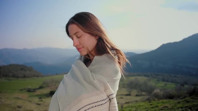 Joyful charming young female wrapping up in organic plaid and protected from country wind, cheerful emotions and lonely freedom feeling at wonderful Europe nature, portrait of no make-up smiling girl