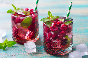 Raspberry cocktail, fizz, lemonade, ice tea with fresh mint on blue wooden background. Close up.
