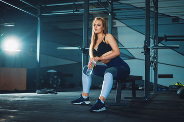 Fototapeta na wymiar Young attracrive sport woman sitting with water bottle on crossfit gym background