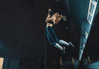 Full length wide angle shot of a woman performing rope climbs at the gym.  Copyspace background with athletics healthy composition. Crossfit and fitness - Powered by Adobe