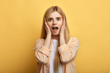 emotional beautiful fair-haired woman screaming with shock,, holding hands on her cheeks. close up photo. isolated yellow background. studio shot.emotion and feeling