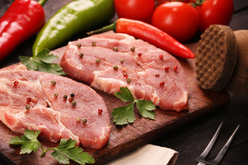 Raw meat. Raw pork steak on a cutting board with vegetables, peppers, tomato, salt and spices on a black background
