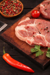 Raw meat. Raw pork steak on a cutting board with vegetables, peppers, tomato, salt and spices on a black background
