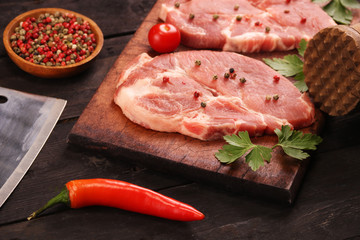 Raw meat. Raw pork steak on a cutting board with vegetables, peppers, tomato, salt and spices on a black background