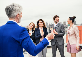 A group of joyful businesspeople having a party outdoors on roof terrace in city.