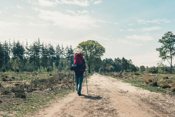 Fototapeta premium Young man in red backpack walking on dirt road on sunny day.