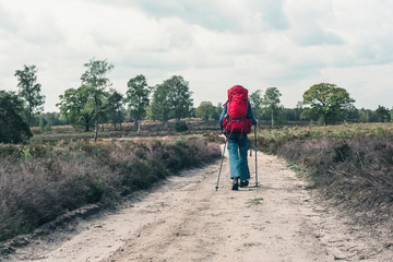 Backpacker going downhill on dirt road under cloudy sky.