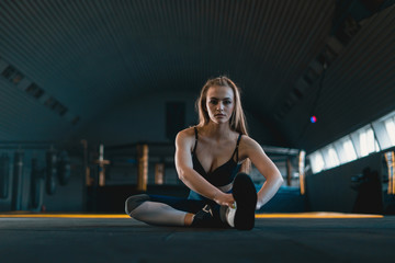 Fototapeta na wymiar Stretching gymnast girl doing warming exercizes. View of attractive young woman doing sports at crossfit gym