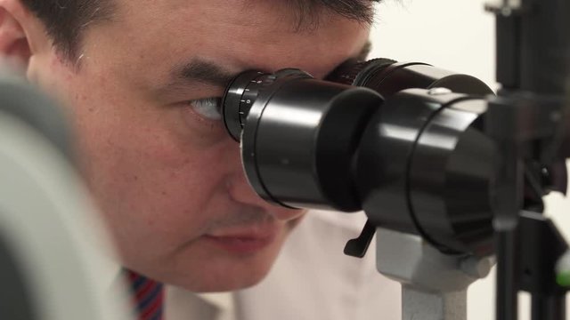 A professional doctor performing eyesight check-up using modern slit lamp. A close-up front shot of an opticians face during examination of patient