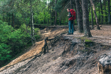 Young man with red backpack at edge of canyon in spring forest.