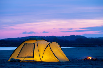 Camping with yellow tent at sunrise on a sand river bank