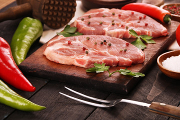 Raw meat. Raw pork steak on a cutting board with vegetables, peppers, tomato, salt and spices on a black background