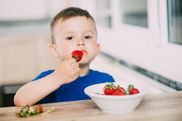 Baby boy in the kitchen eating strawberries very ripe and tasty, stocked with vitamins