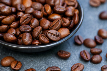 Coffee beans in black bowl on grey slate background. Close up.