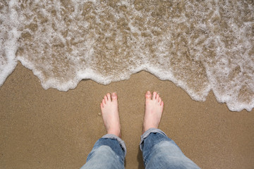 Male feet in jeans on sandy beach. Summer holiday. Beach, feet on sea sand with bubble float wave