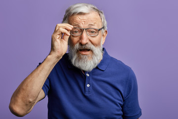 cheerful old man looking through the glasses at the camera isolated on blue background. close up...