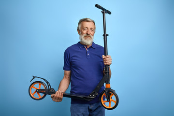 good looking mature man holding scooter and looking at the camera.grandpa preparing present for his grandson on his birthday. old man has bought a scooter for his granddaughter