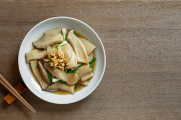 top view of stir fried king oyster mushroom with soy sauce in a ceramic dish on wooden table. asian homemade style food concept.