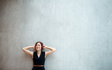 Young business woman with headphones standing against concrete wall in office.