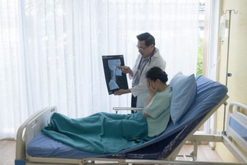 The senior male doctor talked about the patient's illness by explaining the X-ray film in the patient's bed.