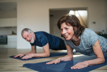 A senior couple indoors at home, doing exercise on the floor.