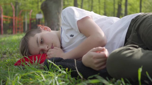 Portrait of a cute boy lying on green grass in spring park. Outdoor recreation.