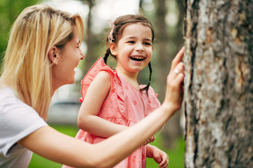 Obraz premium Happy young mother exploring with her cute daughter the nature in the park. Happy family relationship. Woman playing with her child outdoor, exploring the life of nature. Motherhood and childhood.
