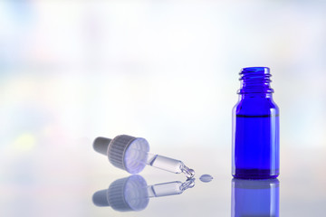 Glass bottle whith dropper on white glass table blue background