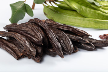 Carob molasses and carob pods (harnup) on white background.