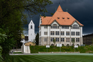 Fototapeta na wymiar Primary school in Brugg Switzerland. New renovated schoolhouse called Stapferschulhaus with evangelical reformed church in background. School area with soccer field in stormy weather.