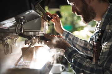 Image closeup of young barista man making coffee while working in cafe or coffeehouse outdoor