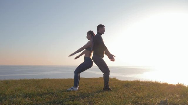 athletic couple back to back simultaneously crouching on a mountain against a beautiful landscape during sunset