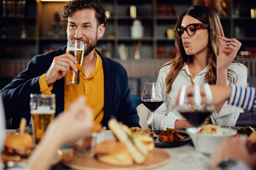 Multiethnic friends sitting at restaurant, drinking alcohol, chatting and having burgers for dinner.