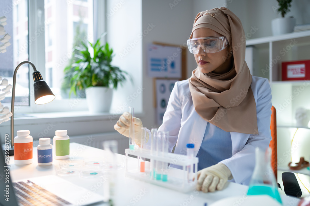 Wall mural busy chemist wearing gloves and glasses sitting and working