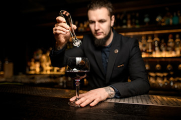 Bartender dropping ice cube in alcohol cocktail