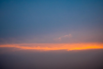 Blue sky with white fluffy clouds, orange rays of light horizontally during sunset.