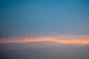Blue sky with white fluffy clouds, orange rays of light horizontally during sunset.