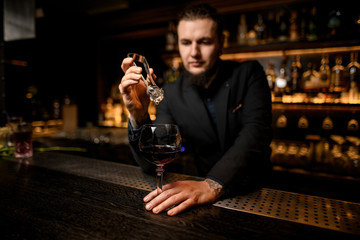 Bartender putting ice cube in alcohol cocktail