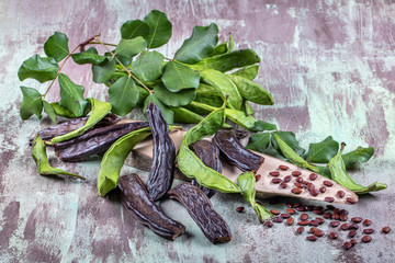 Carob bean(Harnup). Healthy organic sweet carob pods with seeds and leaves on wooden background.