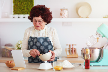 happy mature woman baking with the help of internet, watching recipe on tablet