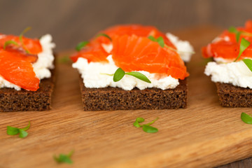 Canape with smoked salmon and cream cheese on wooden board. Selective focus