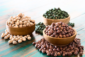 Colored chickpeas (red, green, white) in wooden bowls on rustic background.