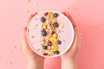 Woman's hands holding smoothie bowl on pink background. Top view, copy space.