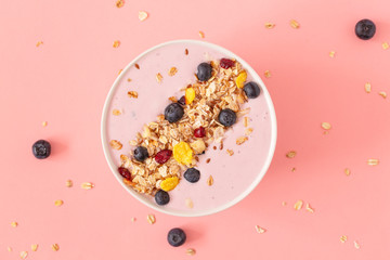 Smoothie bowl with pomegranates, blueberry and granola on a pink background. Tasty and healthy Breakfast. Top view. 