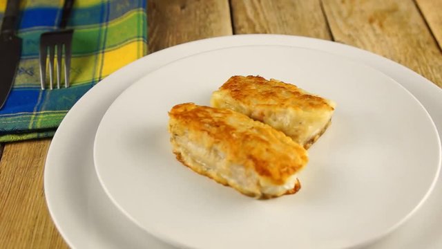 Deep-fried battered cod fillets, in a white plate on a wooden background. Close-up