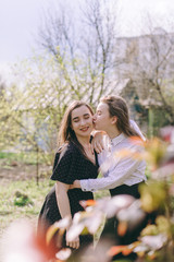 Happy girlfriends at sunset. Portrait of two beautiful young sisters in the green spring garden, hugging in the field in the sunshine. Having fun together, positive emotions, bright colors. Copy space